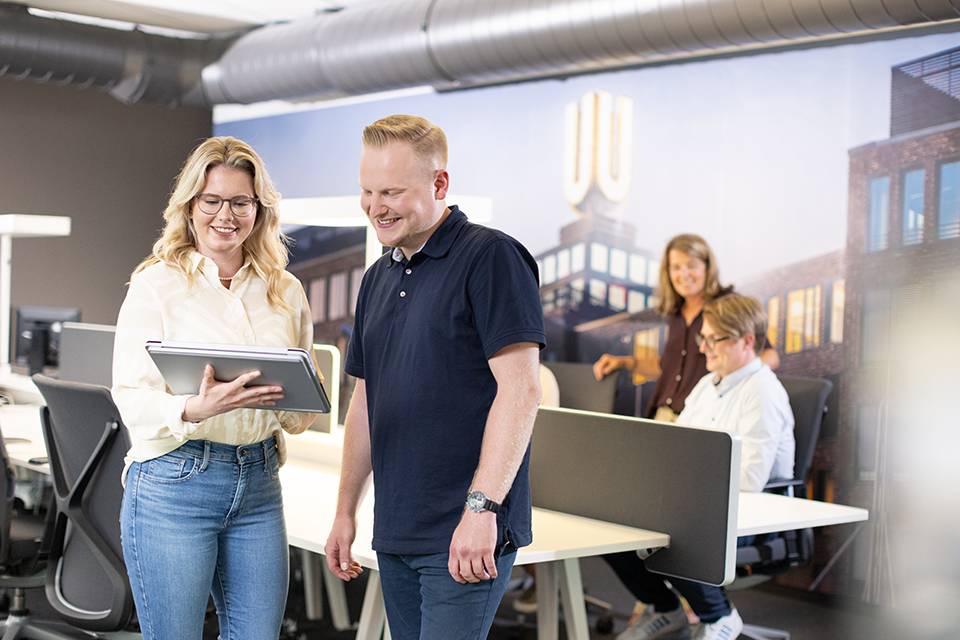 Frau und Mann stehen im Büro und gucken gemeinsam auf IPAD