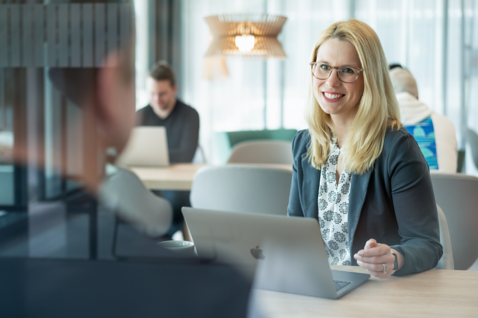 Frau sitzt an eine tisch mit laptop und lächelt ihren gegenüber an
