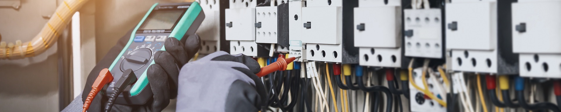 Person misst elektrische Parameter in einem Schaltschrank mit einem Multimeter.