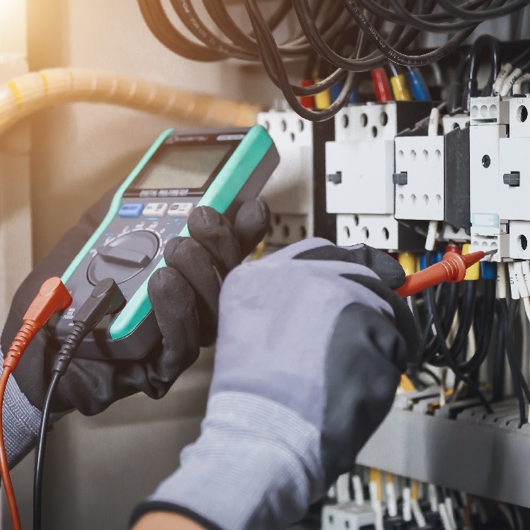 Person misst elektrische Parameter in einem Schaltschrank mit einem Multimeter.