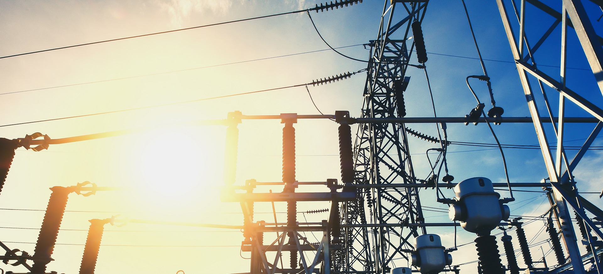 Elektrisches Umspannwerk mit Transformatoren und Hochspannungsleitungen bei Sonnenschein.