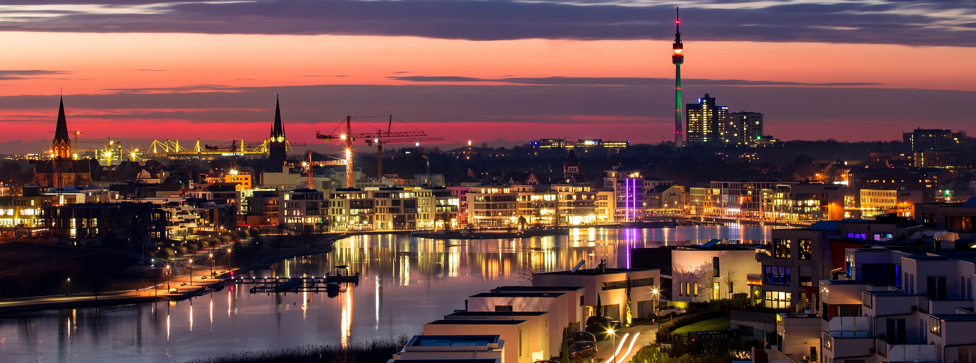 Stadtansicht bei Dämmerung mit Fluss und beleuchtetem Turm.