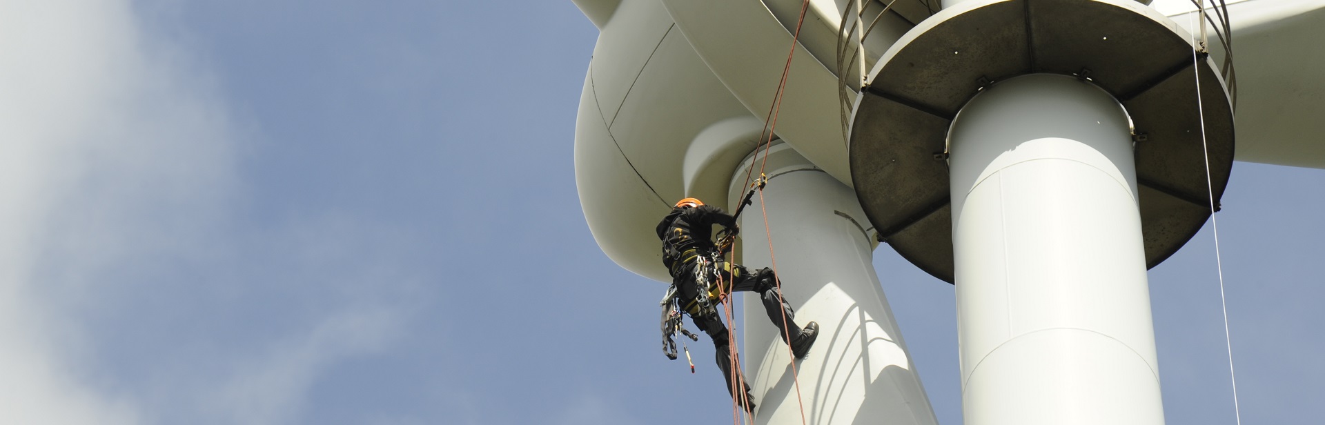 Zwei Personen in Sicherheitsausrüstung warten Windturbine, aufgehängt an Seilen.