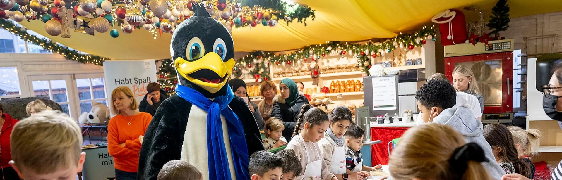 DEW21 Maskottchen Pido, umgeben von Kindern und Weihnachtsdekoration
