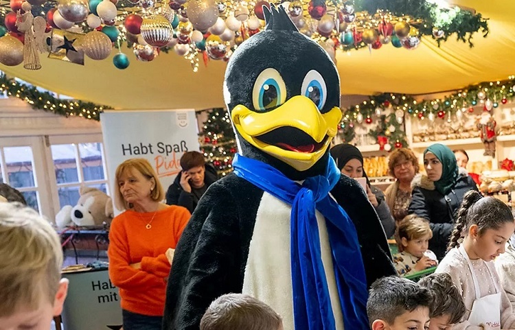 DEW21 Maskottchen Pido, umgeben von Kindern und Weihnachtsdekoration