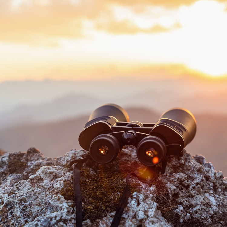 Fernglas auf Felsen vor Berglandschaft und Sonnenuntergang.