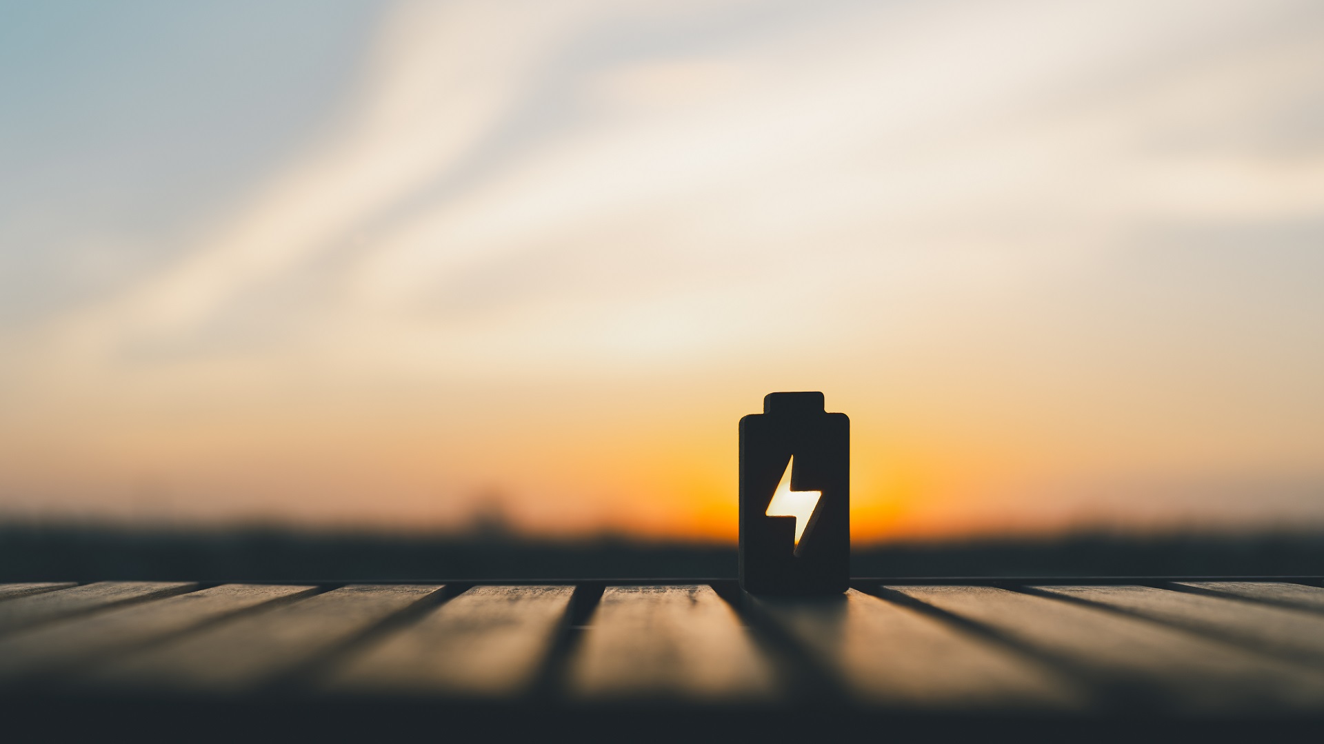 Silhouette eines Batterie-Symbols mit Blitz auf Holzoberfläche, Hintergrund Sonnenuntergang.