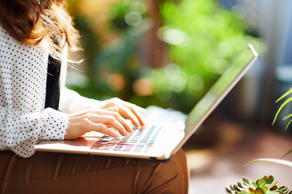 Eine Frau sitzt in ihrem Garten und nutzt ihren Laptop.