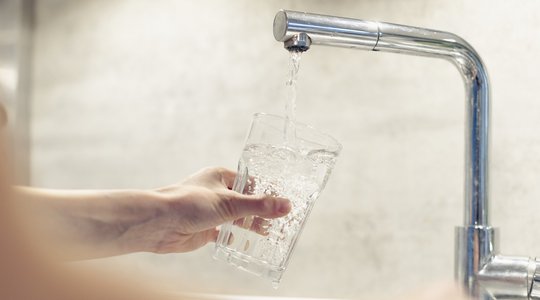 Wasser aus dem Trinkwasserhahn wird in ein Glas gegeben 