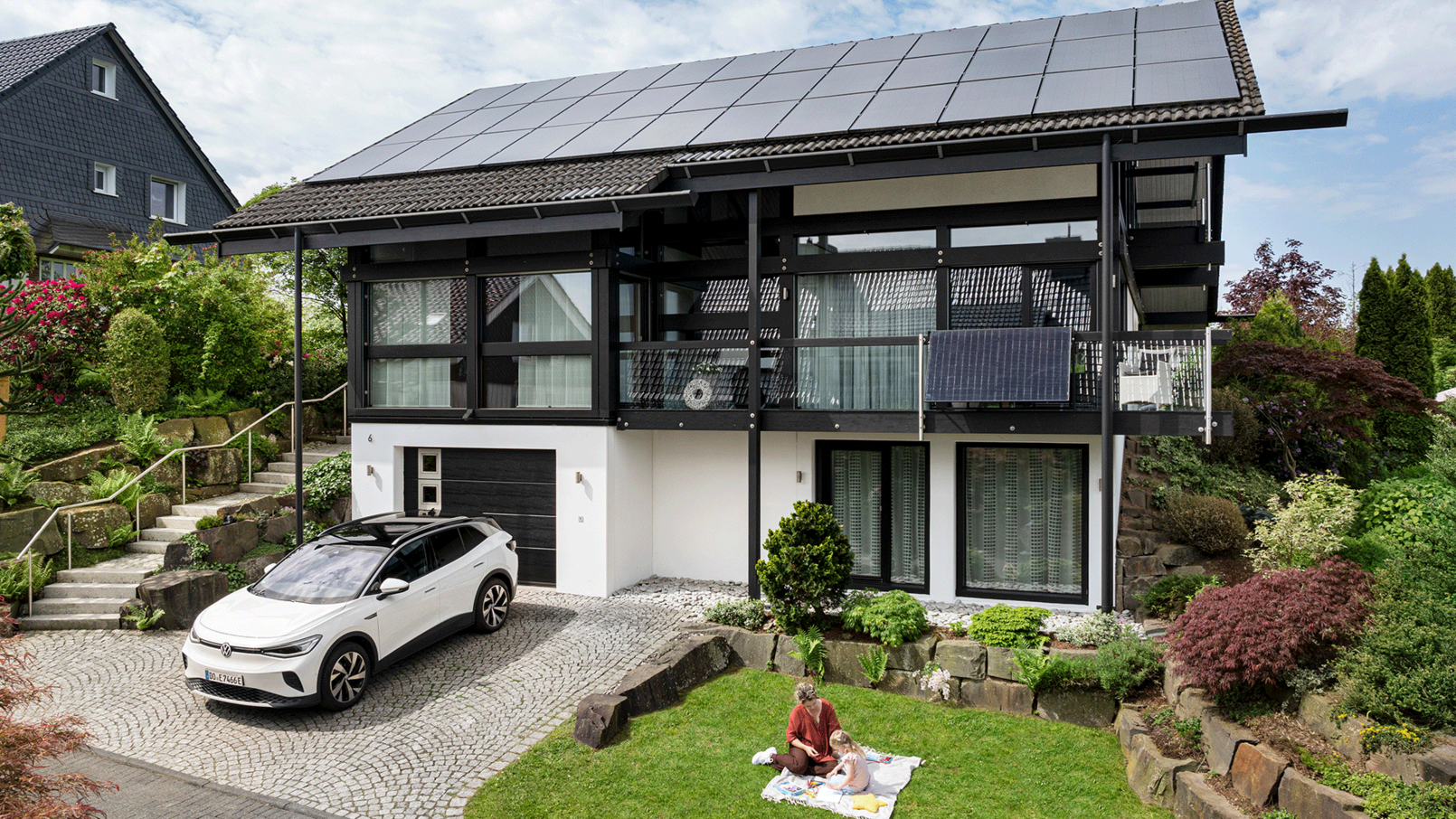 Modernes Haus mit Solardach und E-Auto in Einfahrt, umgeben von Garten und Nachbarhaus