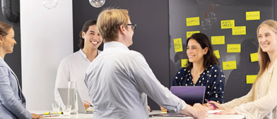 Teammeeting mit Laptop und Notizen vor Wand mit gelben Sticky Notes