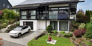Modernes zweistöckiges Haus mit Solarpaneelen, Auto in der Einfahrt, Garten und Person auf Decke.