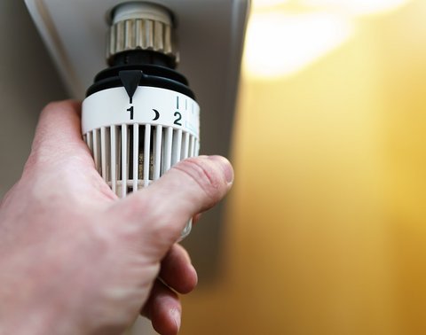 Hand stellt Thermostat am Heizkörper auf Stufe 2.