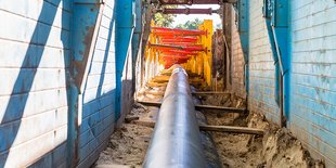 Große Pipeline in Graben, gestützt durch blaue und gelbe Sicherungssysteme.