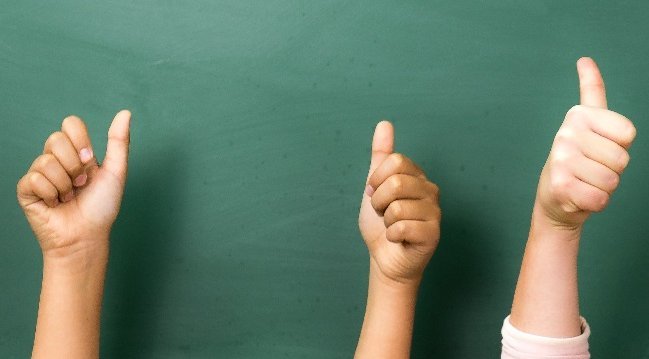 Kinderhände vor einer Schultafel, die den Daumen nach oben zeigen