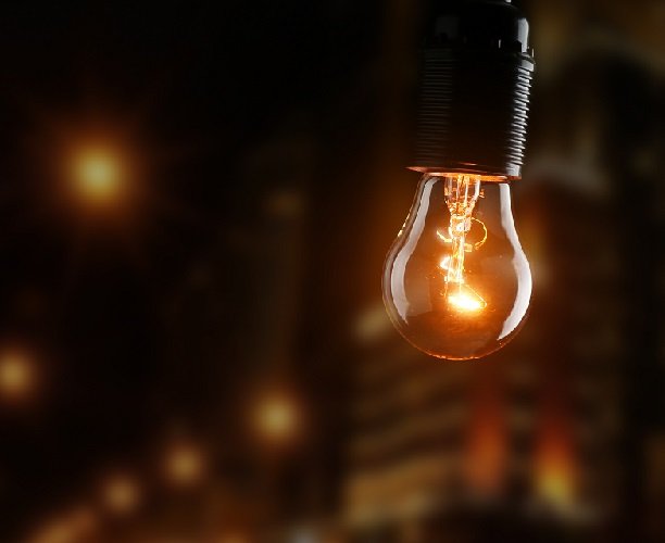 Glühbirne in dunkler Umgebung, mehrere Lichtquellen im Hintergrund.