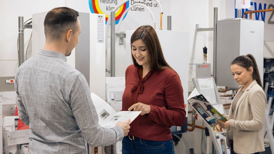 Drei Personen in einem Geschäft oder Showroom, diskutieren oder betrachten Broschüren.