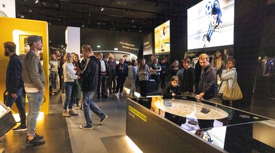 Besucher betrachten ein Stadionmodell und Exponate im Fußballmuseum Dortmund