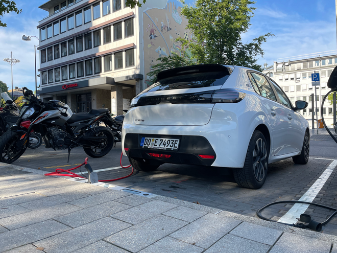 Ladebordstein mit eingestecktem Ladekabel vor Auto auf Stellplatz.