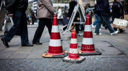 Pylonen stehen auf dem Asphalt im Hintergrund laufen Menschen vorbei