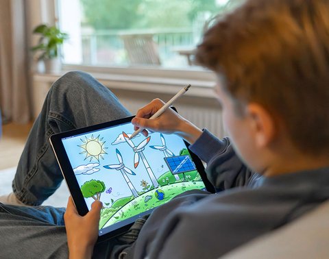 Person auf Couch mit Tablet, zeichnet Windturbinen und Natur mit Stylus.