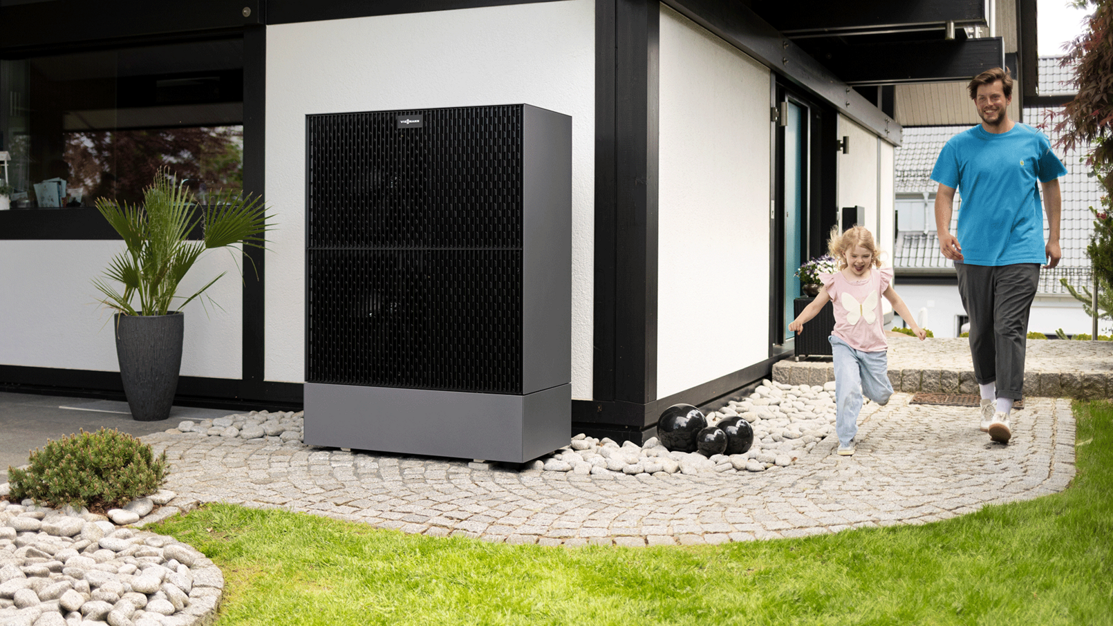 Modernes Haus mit Viessmann-Einheit, daneben ein Erwachsener und ein Kind auf einem Weg.