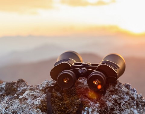 Fernglas auf Felsen vor Berglandschaft und Sonnenuntergang.