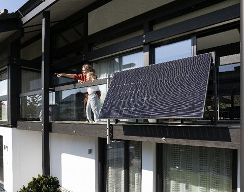 Zwei Personen auf einem Balkon mit Solarpanel, eine Person zeigt in die Ferne.