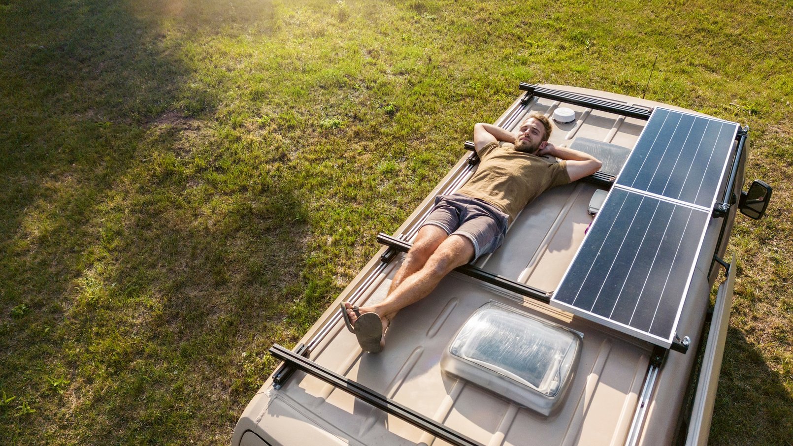 Mann liegt auf einem Wohnwagen, neben ihm eine PV-Anlage auf dem Dach des Wohnmobils