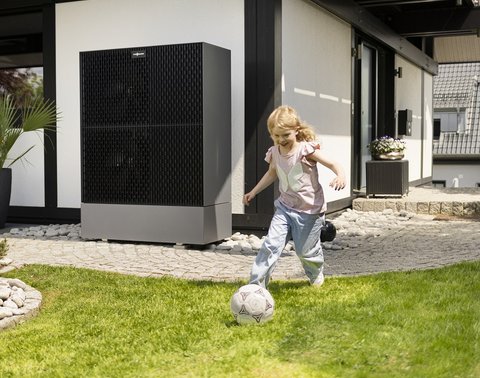 Kind spielt Fußball auf Rasen vor einem modernen Haus mit großen Fenstern.