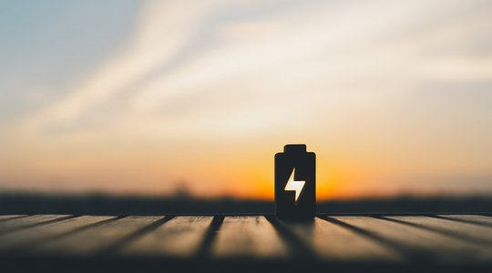 Silhouette eines Batterie-Symbols mit Blitz auf Holzoberfläche, Hintergrund Sonnenuntergang.