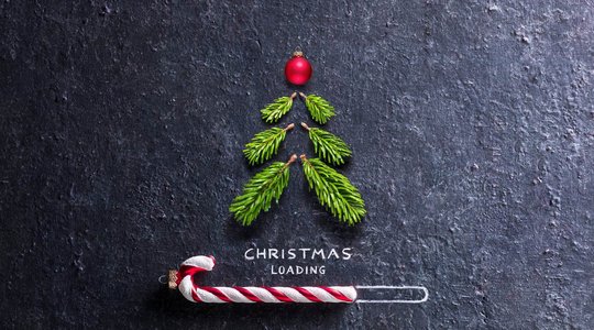 Weihnachtsbaum aus kleinen Zweigen und roter Kugel auf dunklem Hintergrund, darunter "CHRISTMAS LOADING" mit Zuckerstange im Ladebalken.