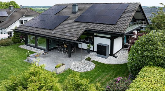 Haus mit Solarpanels auf dem Dach, Garten und möblierter Terrasse.