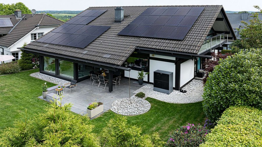 Haus mit Solarpanels auf dem Dach, Garten und möblierter Terrasse.