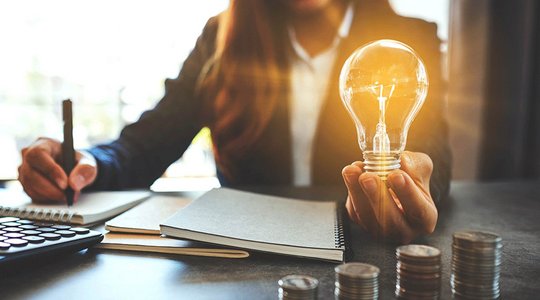 Leuchtende Glühbirne Modernes Haus mit Solardach und E-Auto in Einfahrt, umgeben von Garten und Nachbarhaus