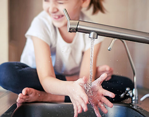Ein Kind wäscht sich in der Küche die Hände am Waschbecken.